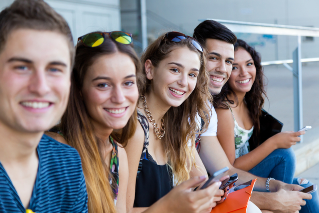 Portrait of group of students having fun with smartphones after class.