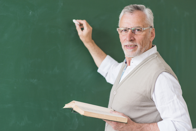 senior male teacher holding book writing blackboard