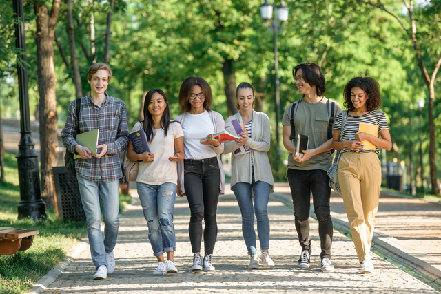 Picture of multiethnic group of young cheerful students walking while talking. Looking aside.